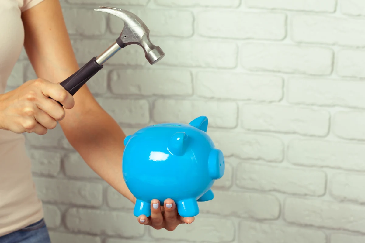 Une femme qui casse sa tirelire avec un marteau pour financer des travaux de rénovation